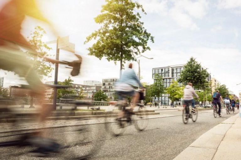 Radfahrer fahren in einer urbanen Umgebung, Bäume und moderne Gebäude im Hintergrund.