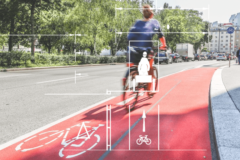 Radfahrer auf einem roten Radweg in einer Stadt, Umgebungsvegetation im Hintergrund.