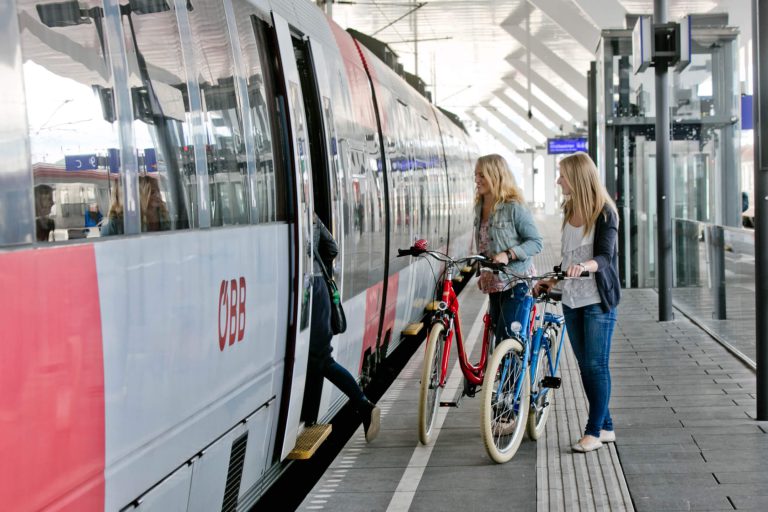Fahrradmitnahme im Zug: zwei Frauen mit Fahrrädern am Bahnsteig vor einem ÖBB-Zug.