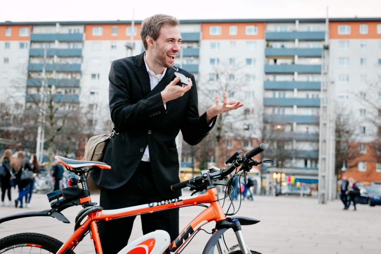 Mann im Anzug spricht am Handy neben seinem Fahrrad in urbaner Umgebung.