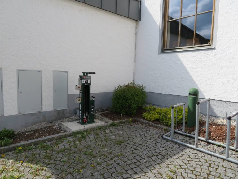 Radservicestation neben einer Wand, umgeben von Pflanzen und Pflastersteinen.