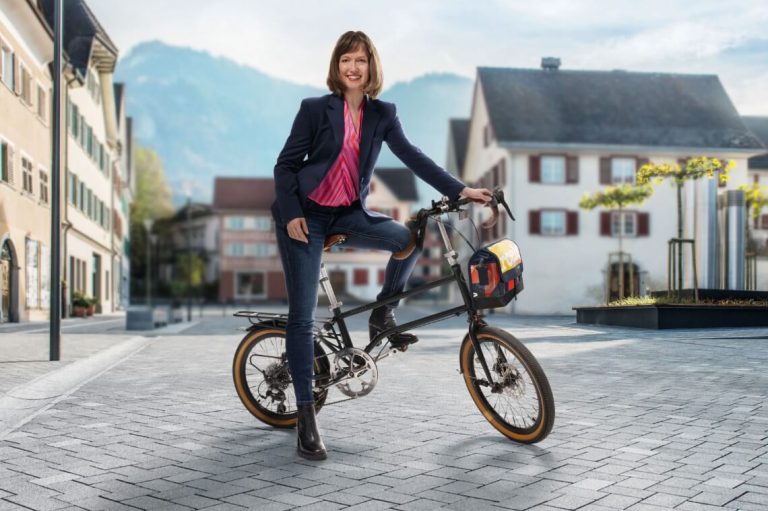 Frau auf einem Lastenrad in einer Stadtlandschaft, Thema nachhaltige Mobilität.