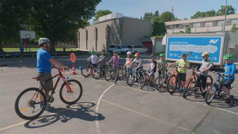 Kinder bei AUVA-Radworkshop mit Trainer, Fahrräder und Helmchecks im Geschicklichkeitsparcours.