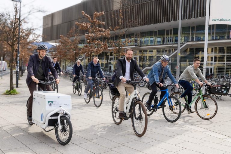 Fahrradfahrer mit Lastenrad und E-Bikes in urbaner Umgebung, Förderung nachhaltiger Mobilität.
