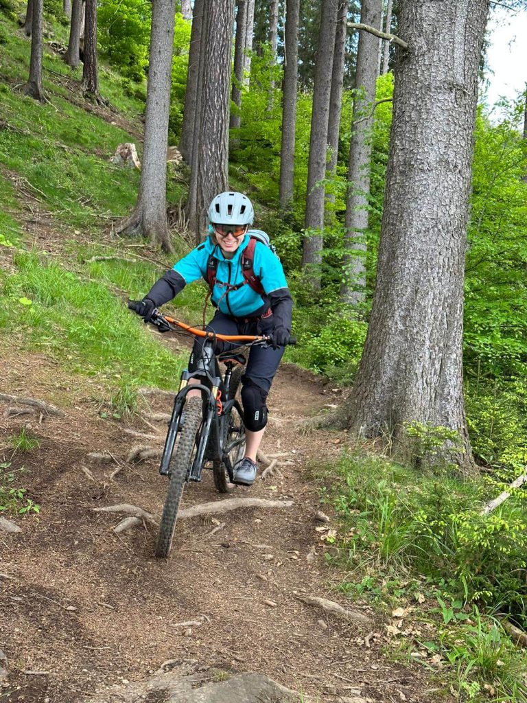 Radfahrerin auf einem Waldweg, umgeben von Bäumen und grüner Natur, beim Fahren.