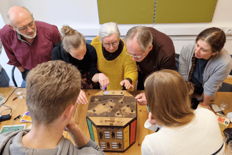 Teilnehmer:innen eines Workshops arbeiten gemeinsam an einem interaktiven Spiel auf einem Tisch.