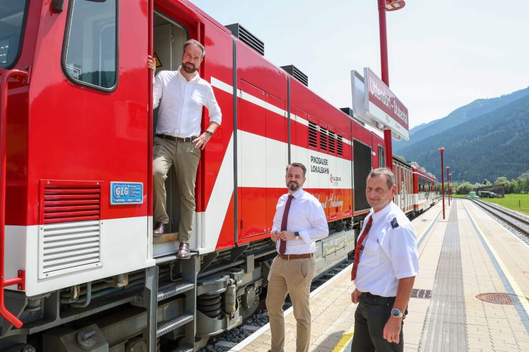 Eisenbahnpersonal an der Pinzgauer Lokalbahn am Bahnhof, mit Berglandschaft im Hintergrund.
