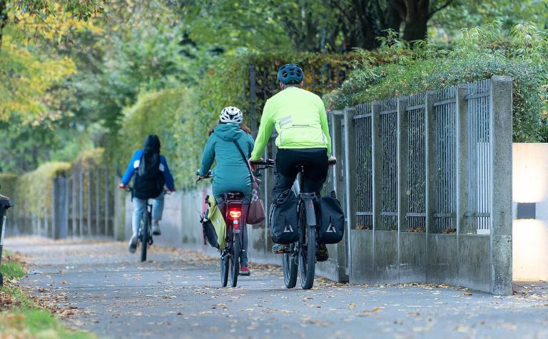 Zwei Radfahrer auf einem Spazierweg, umgeben von Bäumen und einer Mauer in Salzburg.