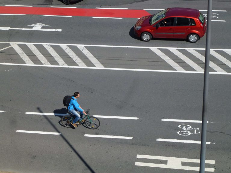 Pendler radelt auf Fahrradweg in der Stadt, umweltfreundliche Mobilität fördern.