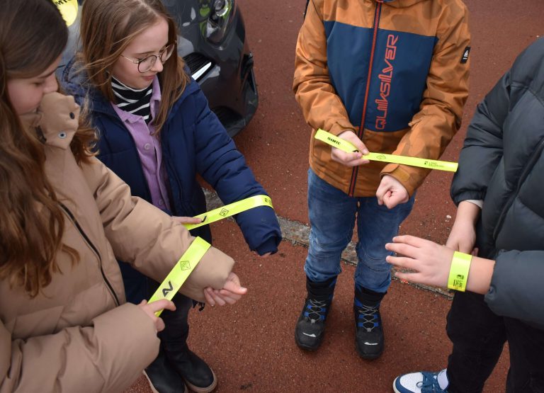 Kinder binden sich gelbe Armbänder bei einem Rad-Event zur Förderung von Verkehrssicherheit.