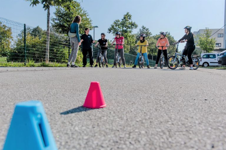 Fahrradtraining mit Jugendlichen und Trainerin auf Asphalt, bunte Hütchen im Vordergrund