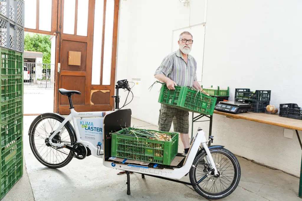 Mann lädt grüne Gemüsekisten auf ein weißes Lastenrad