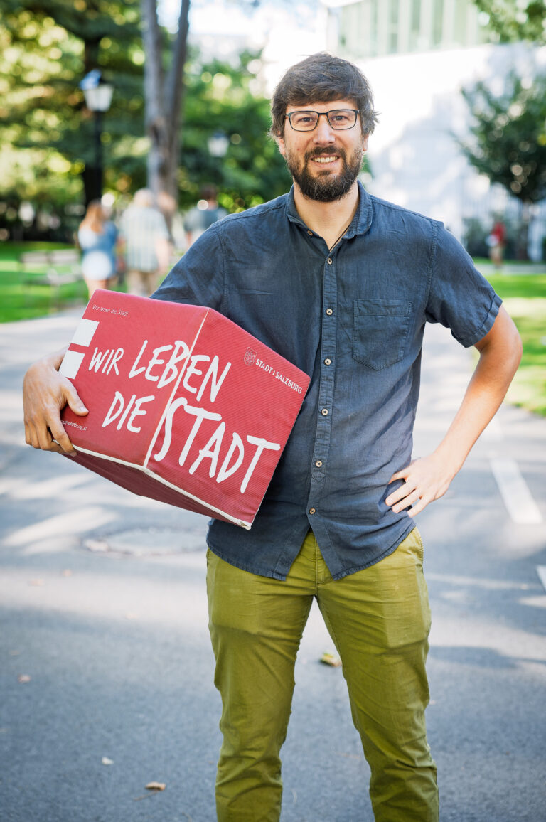 Mann mit Brille hält roten Karton mit Aufschrift Wir leben die Stadt
