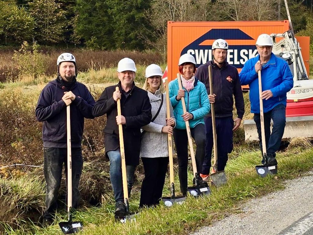 Sechs Personen mit Spaten und Helmen beim Spatenstich im Freien