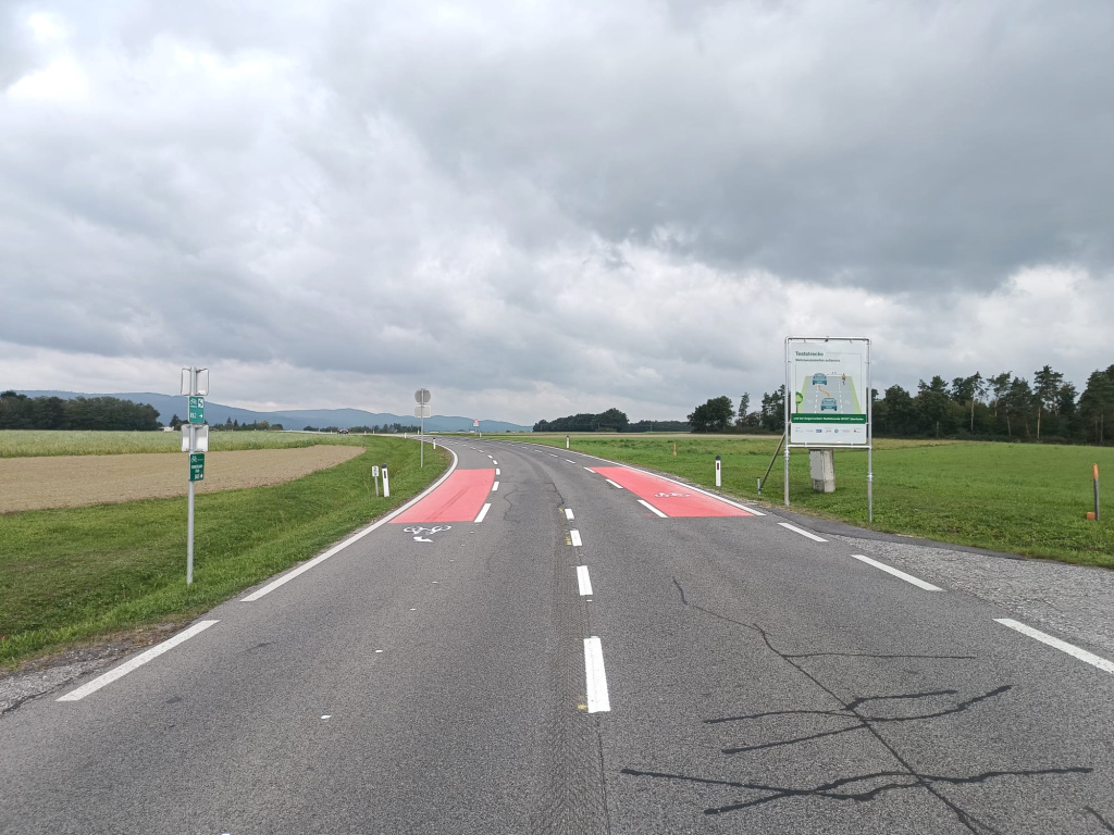 Landstraße mit rot markierten Radstreifen in ländlicher Umgebung unter bewölktem Himmel