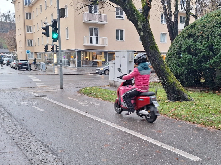 E-Moped eines Essenszustellers auf einem Radweg an einer Kreuzung in Salzburg
