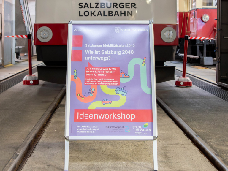 Aufsteller mit Plakat zum Ideenworkshop für den Salzburger Mobilitätsplan 2040 in einer Lokalbahn-Halle