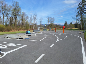 Asphaltierter Rad-Parcours mit Fahrbahnmarkierungen, Rampe, Stoppschild und mehreren Kindern im Freien