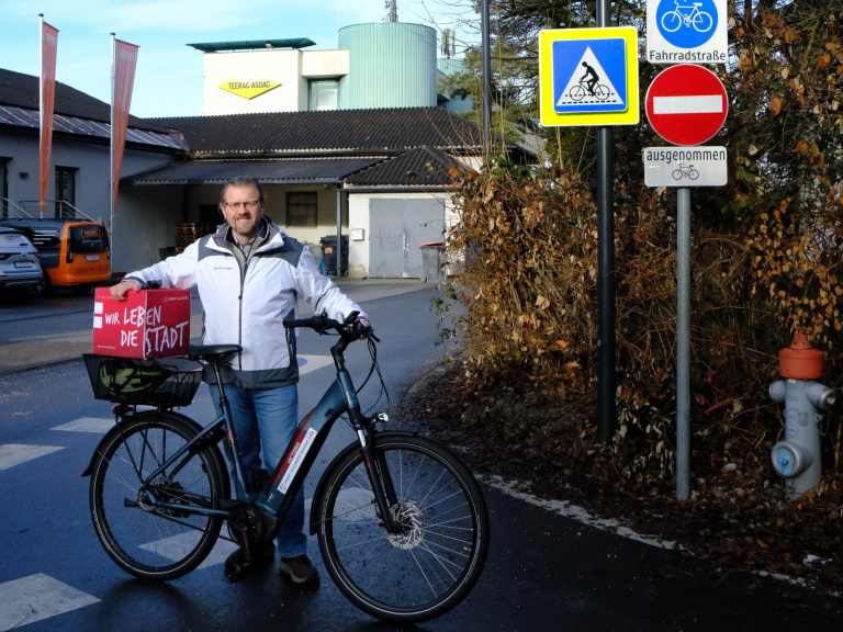 Markus Huber steht mit einem Fahrrad neben Straßenschildern für Fahrradstraße und Radquerung