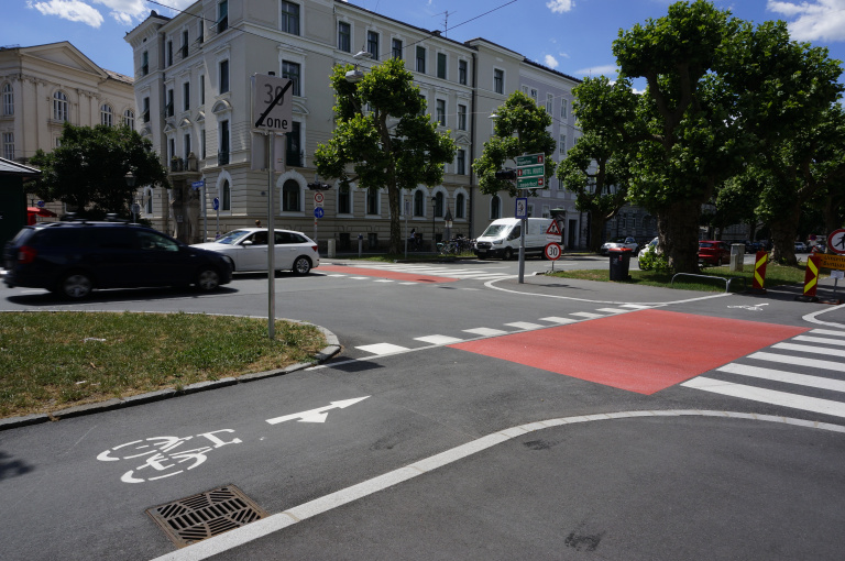 Rote Radfurt an einer Kreuzung in Salzburg mit 30-Zone-Schild, Autos, Bäumen und historischen Häusern
