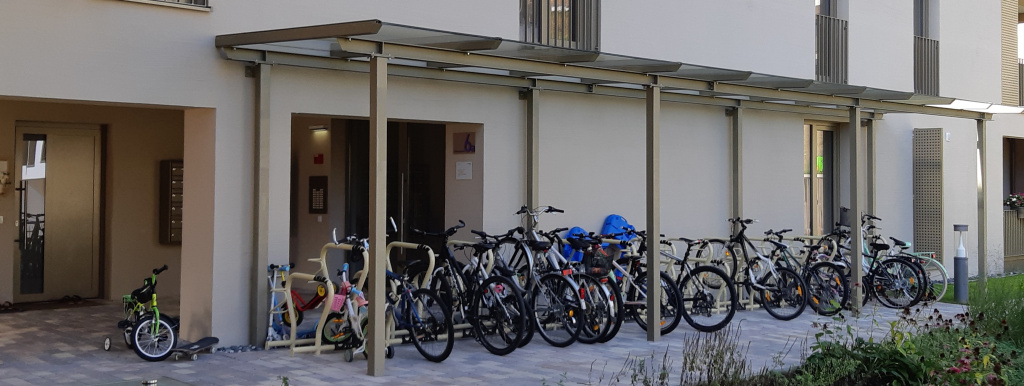 Überdachte Fahrradständer mit vielen Rädern und Kinderfahrrädern vor einem Wohngebäude