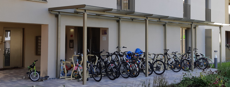 Überdachte Fahrradständer mit vielen Rädern und Kinderfahrrädern vor einem Wohngebäude